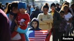 María Orellana (28 años), a la izquierda, y su hijo de siete años Ángel (sosteniendo una bandera), ambos hondureños, son parte de una caravana de miles de migrantes centroamericanos que hacen fila afuera de un refugio temporal en Tijuana, México, el 25 de noviembre de 2018.