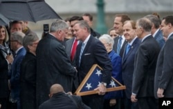 Sen. Richard Burr, R-N.C., holding the flag, reaches out to shake hands with Rev. Franklin Graham, the son of the late Rev. Billy Graham, on the East Front of the U.S. Capitol in Washington.