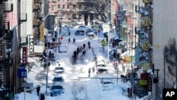 People clear snow from parked cars on Henry Street in the Chinatown neighborhood in New York, Jan. 24, 2016.