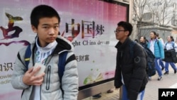 2018年3月12日，北京一所學校外面，青少年走過宣傳牌，牌上寫著中英文口號“點亮中國夢 知識改變命運 付出收獲財富”。