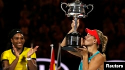 Germany's Angelique Kerber kisses the trophy as Serena Williams of the U.S. claps after Kerber won their final match at the Australian Open tennis tournament at Melbourne Park, Australia, Jan. 30, 2016. 