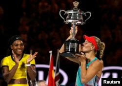 Germany's Angelique Kerber kisses the trophy as Serena Williams of the U.S. claps after Kerber won their final match at the Australian Open tennis tournament at Melbourne Park, Australia, Jan. 30, 2016.