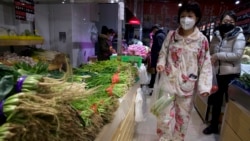 A woman wearing a mask and pajamas shop for vegetables at a store in Beijing, China on Tuesday, Feb. 18, 2020. (AP Photo/Ng Han Guan)