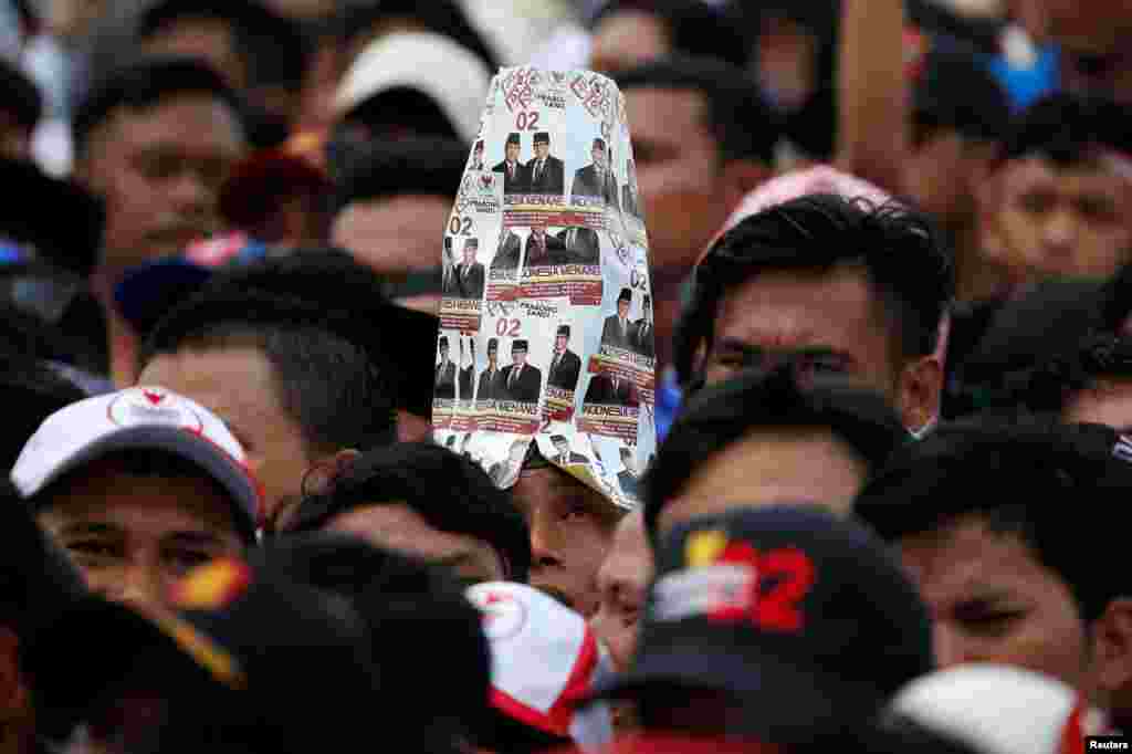 A supporter wears a hat made of pictures of Indonesia&#39;s presidential candidate for next month&#39;s election Prabowo Subianto and his running mate Sandiaga Uno, during a campaign rally in Bogor, West Java province.