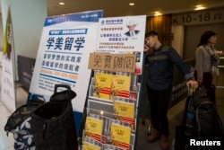 Seorang mahasiswa China berbicara di telepon di belakang poster iklan pendidikan luar negeri usai ujian SAT (Scholastic Assessment Test) di AsiaWorld-Expo, Hong Kong, 2 November 2013. SAT adalah pra syarat mendaftar ke perguruan tinggi AS. (Foto: Reuters)