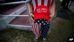 FILE - A man dressed in American flag clothes holds "Make America Great Again" hats at a December 2016 rally in Mobile, Alabama.