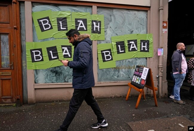 FILE - A man walks past a shop with the phrase used by climate activist Greta Thunberg on it's windows as a protest organized by the Cop26 Coalition passes by in Glasgow, Scotland, Nov. 6, 2021.