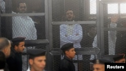 FILE - Political activists Ahmed Maher (R), Ahmed Douma (C) and Mohamed Adel, founder of 6 April movement, look on from behind bars in Abdeen court in Cairo, December 2013.