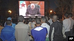 People listen to the speech of Algeria's President Abdelaziz Bouteflika on a giant television screen in Algiers, April 15, 2011