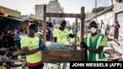 Des employés municipaux portant des masques comme mesure préventive contre le coronavirus nettoient les étals d'un marché informel au quartier populaire de la Médina à Dakar, le 22 mars 2020. (Photo: JOHN WESSELS / AFP)