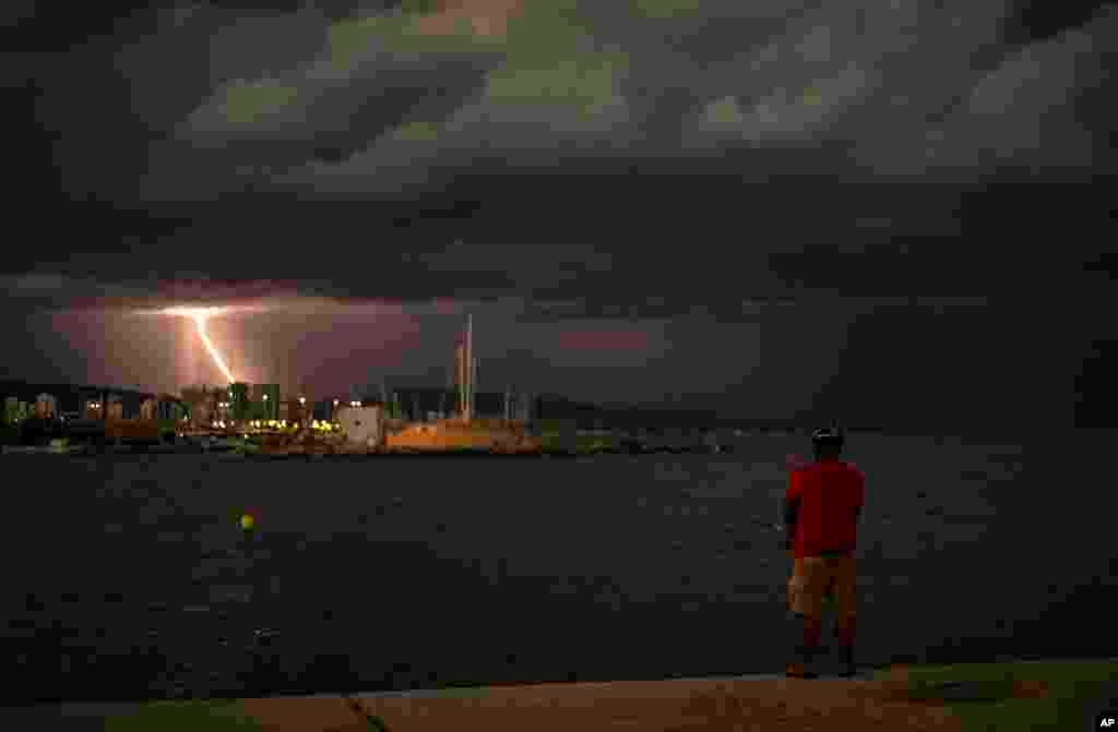 A man is fishing as lightning flashes in the night sky during a storm in Barcelona, Spain, Aug. 30, 2020.