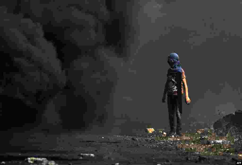 A Palestinian demonstrator watches as smoke billows from a fire during clashes with Israeli forces following a weekly protest against the expropriation of Palestinian land by Israel, in the village of Kfar Qaddum, in the Israeli-occupied West Bank.