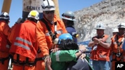 In this photo released by the Government of Chile, miner Omar Reygadas Rojas, kneeling in green, embraces his son after being rescued from the collapsed San Jose gold and copper mine, near Copiapo, Chile, Wednesday, Oct. 13, 2010.