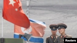 在中朝边界鸭绿江的朝鲜新义州岸边停泊的一艘船上，朝鲜士兵在朝鲜国旗与中国国旗前站岗。 （2013年6月10日）