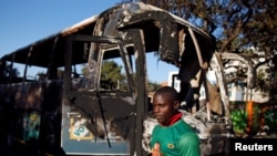 A supporter of the ruling ZANU-PF walks past a burnt vehicle at the party's offices a day after the clashes between security forces and opposition protesters in Harare, August 2, 2018. 