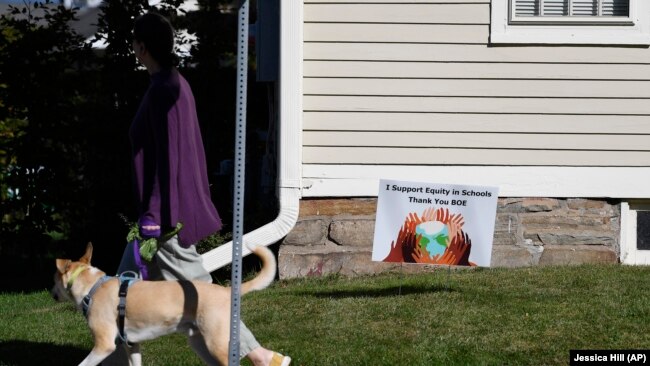 A woman walks her dog past a sign supporting equity in schools, in Guilford, Conn., on Tuesday, Oct. 19, 2021. (AP Photo/Jessica Hill)