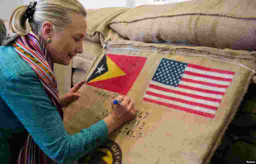U.S. Secretary of State Hillary Clinton (C) autographs a sack of coffee beans with the flags of East Timor and the U.S. , at the Timor Coffee Cooperative in Dili September 6, 2012. 