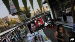 In this photo taken on Feb 23, 2012, people walk past a roadside stall selling the posters of Burmese democracy icon Aung San Suu Kyi and her late father in Rangoon, Burma. 