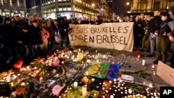 People hold a banner reading "I am Brussels" behind flowers and candles to mourn for the victims at Place de la Bourse in the center of Brussels, March 22, 2016.