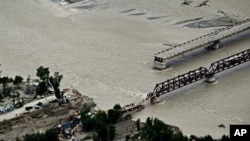 Flood survivors cross a hastily-repaired bridge next to a main bridge swept away by flood waters in Swat Valley, 10 Aug 2010