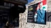 FILE - A man on a motorcycle rides past a poster depicting Syria's President Bashar al-Assad on a wall in the pro-government al-Zahraa neighbourhood in Homs, May 15, 2014.