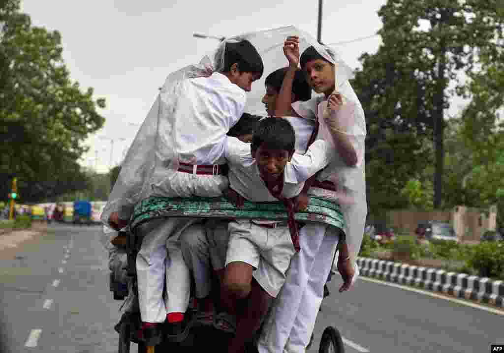 Học sinh Ấn Độ dùng một tấm vải nhựa để giữ cho khỏi ướt khi đi trên một chiếc xe kéo lúc trời mưa nhẹ ở New Delhi