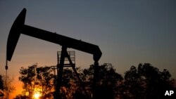 FILE - The sun sets behind an oil well in a field near El Tigre, within the Hugo Chavez oil belt in Venezuela, Feb. 19, 2015.