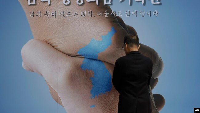 Một người đàn ông xem tấm biểu ngữ có in hình bản đồ bán đảo Triều Tiên và thông điệp bày tỏ mong muốn cuộc họp thượng đỉnh sẽ thành công. bày tỏ mong muốn cuộc họp thượng đỉnh thành công.