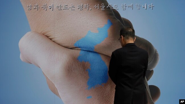 Một người đàn ông xem tấm biểu ngữ có in hình bản đồ bán đảo Triều Tiên và thông điệp bày tỏ mong muốn cuộc họp thượng đỉnh sẽ thành công. bày tỏ mong muốn cuộc họp thượng đỉnh thành công.