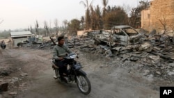Cảnh sát Miến Điện cưỡi xe máy qua các căn nhà và xe cộ bị phá hủy trong các vụ bạo động sắc tộc giữa Phật giáo và Hồi giáo tại Meikhtila, ngày 25/3/2013.