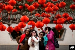 Chinese women share a light moment as they take a selfie near a tree decorated with red lanterns ahead of the Chinese Lunar New Year at Ditan Park in Beijing, Jan. 30, 2019.