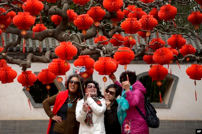 Chinese women share a light moment as they take a selfie near a tree decorated with red lanterns ahead of the Chinese Lunar New Year at Ditan Park in Beijing, Jan. 30, 2019.