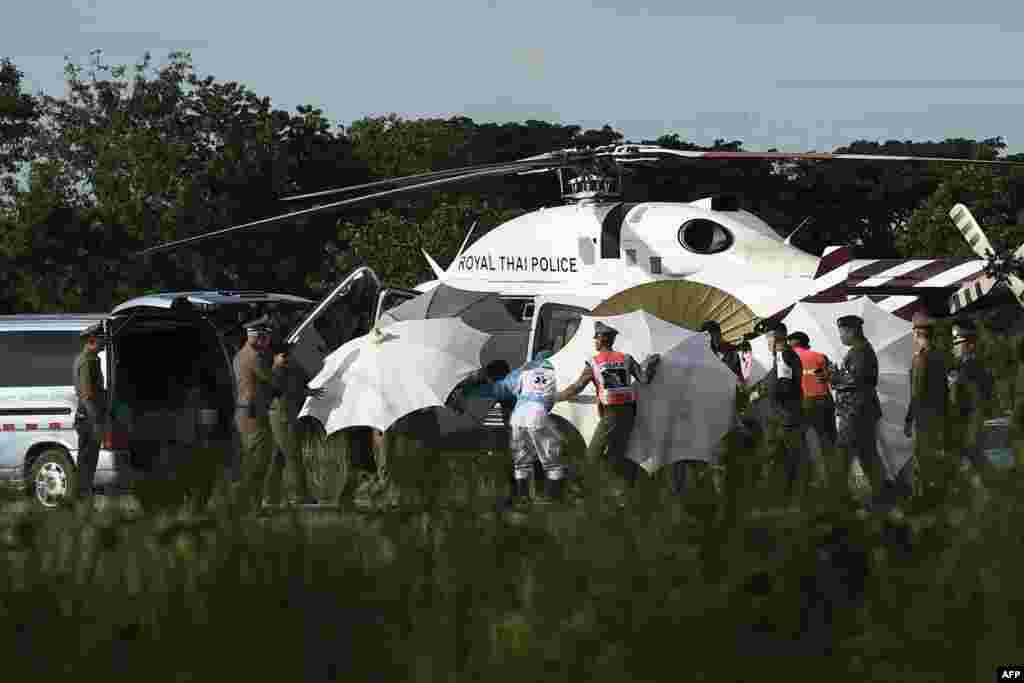 Police and military personnel use umbrellas to cover around a stretcher near a helicopter and an ambulance at a military airport in Chiang Rai as rescue operations continue for those still trapped inside the cave in Khun Nam Nang Non Forest Park in the Mae Sai district, Thailand.