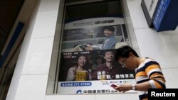 FILE - A man checking his smartphone walks past a bank advertisement in Hong Kong, China, Nov. 30, 2015. Recent research indicates that outlay on digital advertising in China has surpassed the amount spent on traditional ads.