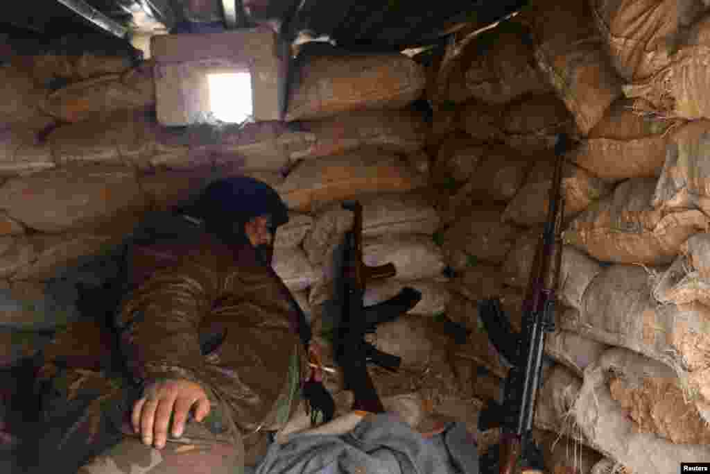 A rebel fighter rests with his weapons behind sandbags at insurgent-held al-Rashideen, Aleppo province, Syria, Dec. 30, 2016. ជនសកម្មប្រយុទ្ធរបស់ក្រុមឧទ្ទាមម្នាក់កំពុងសម្រាកនៅជិតកាំភ្លើងនៅខាងក្រោយបាវដីខ្សាច់ នៅតំបន់ al-Rashideen ដែលកាន់កាប់ដោយពួកបះបោរ នៅក្នុងក្រុង Aleppo។