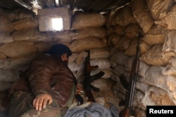 一个反政府武装战士在他们控制的阿勒颇省拉希迪恩的沙袋背后携带武器休息(2016年12月30日)