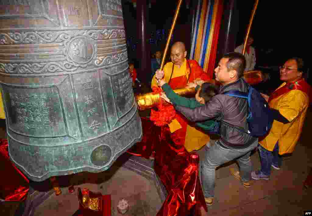 2018年12月31日，在中国海南省三亚的一座寺庙里，游客和僧人在新年前夕撞钟祈福，大钟上有“国泰民安”字样。
