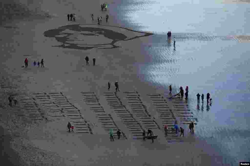 People gather to look at an Armistice day sand portrait of Imperial Military Nurse Rachel Ferguson who died in June 1918 during World War I, created as part of Danny Boyle&#39;s Pages of The Sea celebrations, on Downhill Beach in Coleraine, Northern Ireland.