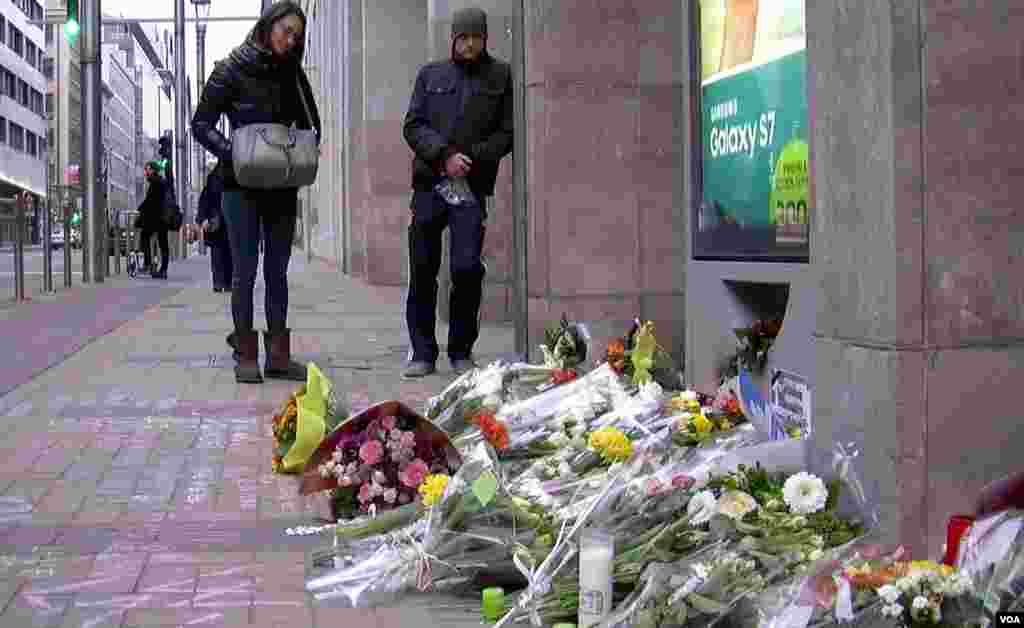Bystanders look at the flowers and candles set out as a memorial outside the Moelenbeek metro station in Brussels, March 24, 2016. (L. Bryant/VOA)