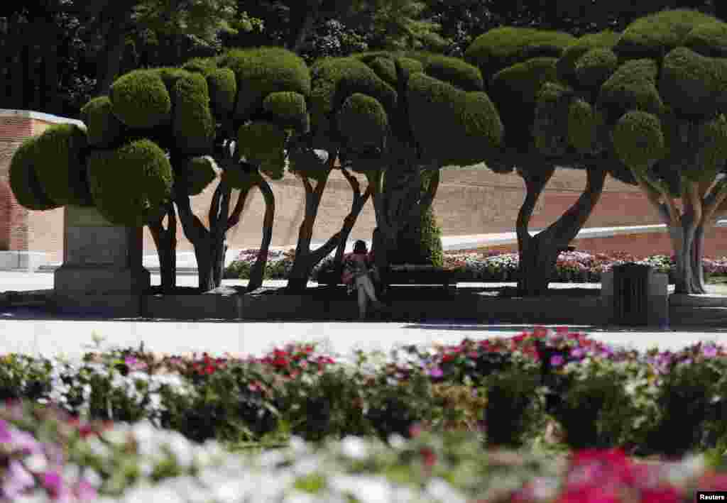 A woman listens to music as she sits on a bench during a hot summer day at Madrid's El Retiro park, Spain.