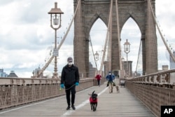 People wear facial masks for protection against the coronavirus as they walk their dogs on the Brooklyn Bridge, Friday, April 10, 2020, in New York. (AP Photo/Mary Altaffer)