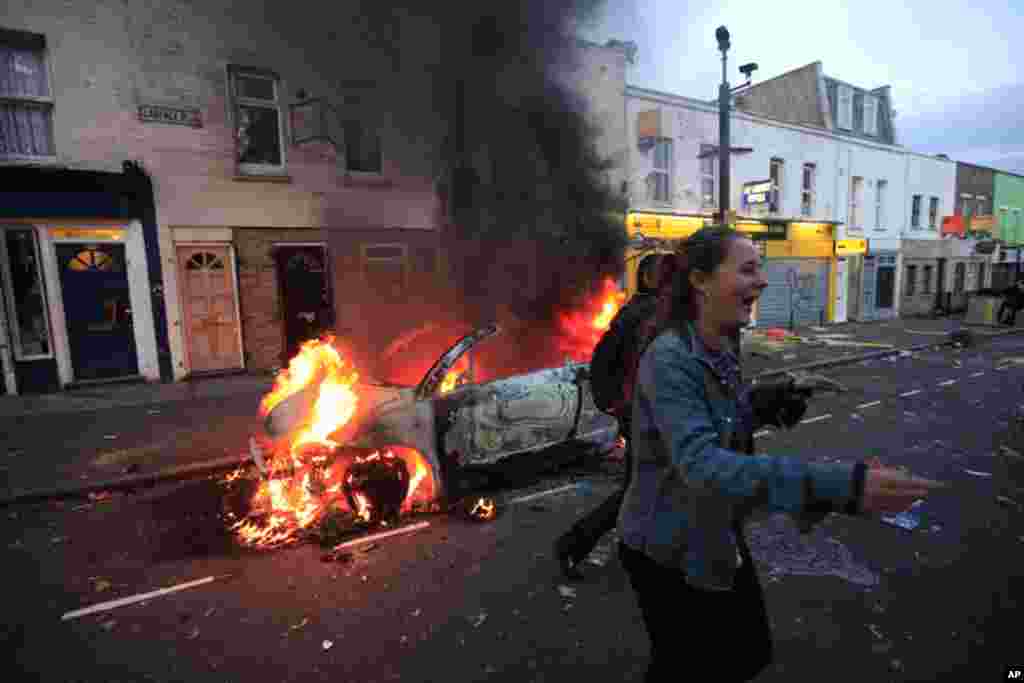 A girl jokes as a car burns after it was set on fire by rioters in Hackney, east London, Monday Aug. 8, 2011. Youths set fire to shops and vehicles in a host of areas of London _ which will host next summer's Olympic Games _ and clashed with police in th