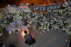 A protester lights candles near flowers and a banner that reads "From all of us - God bless Chow Tsz-Lok" at the site where he fell during a recent protest in Hong Kong, Nov. 8, 2019.