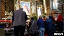 Católicos oran en una iglesia en Roma frente a una imagen del papa Juan Pablo II.