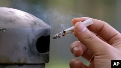 FILE - A smoker discards a cigarette into a container at a designated smoking location in Seattle, Wash., Oct. 17, 2015.