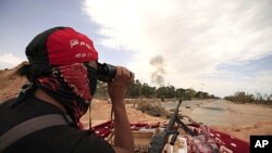 A Libyan rebel fighter uses a pair of binoculars as smoke rises from an explosion at Misrata's western front line June 11, 2011. The cause of the explosion was unclear.