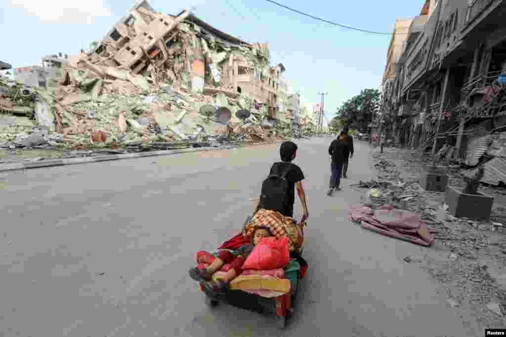 A Palestinian boy pulls a cart carrying his brother and their belongings as they flee their home during Israeli air and artillery strikes, near the site of a tower building destroyed in earlier strikes in Gaza City.