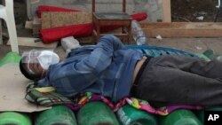 A man sleeps on top of empty oxygen cylinders, waiting for a shop to open to refill his tank, in Lima early Feb. 18, 2021, as the lack of medical oxygen to treat COVID-19 patients continues to be the norm in Peru.