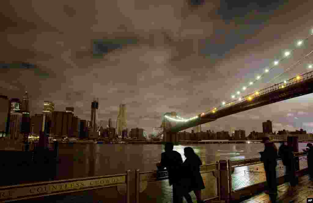 People stop along the Brooklyn waterfront to look at the Brooklyn Bridge and the Manhattan skyline, Oct. 30, 2012 in New York.