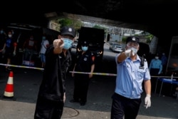 FILE - Police and security personnel direct a photographer to refrain from taking pictures at a a cordon isolating a residential area near Xinfadi market, a new coronavirus hotspot in Beijing, China, June 20, 2020.